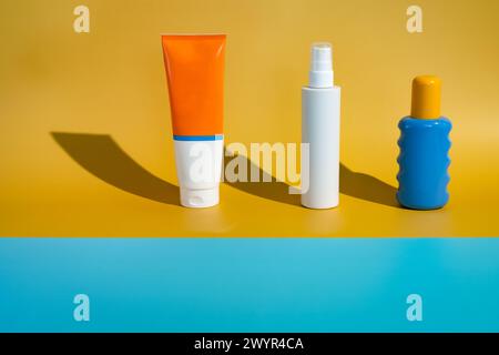 Verschiedene leere Sonnenschutzverpackungsflaschen auf minimalistischem Strand aus gelbem und blauem Papier in direkter Sonneneinstrahlung. Modell-Vorlage für Hautschutz für den Sommer Stockfoto