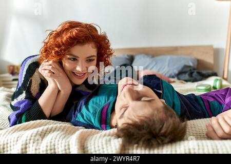 Rothaarige verführerische Frau, die ihren hübschen Freund liebevoll anschaut, während sie zusammen auf dem Bett liegt Stockfoto