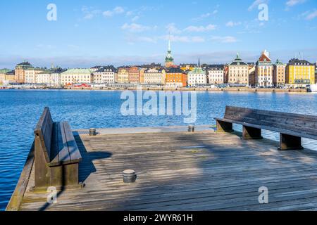 Ein Panoramablick von einem hölzernen Pier zeigt die lebhaften Fassaden der Altstadt von Stockholm, die sich im ruhigen Wasser unter einem klaren blauen Himmel spiegeln. Schweden Stockfoto