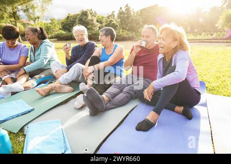 Senioren haben Spaß nach der Yoga-Session, plaudern und trinken heißen Tee im Stadtpark - Reife Freunde lachen zusammen nach der Sportroutine Stockfoto