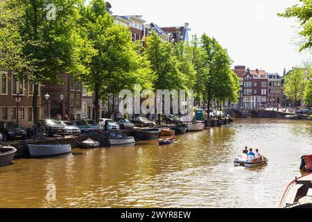 Auf der Keizersgracht segeln die Menschen auf kleinen Freizeitbooten vorbei an den historischen Kanalhäusern im Zentrum von Amsterdam. Stockfoto