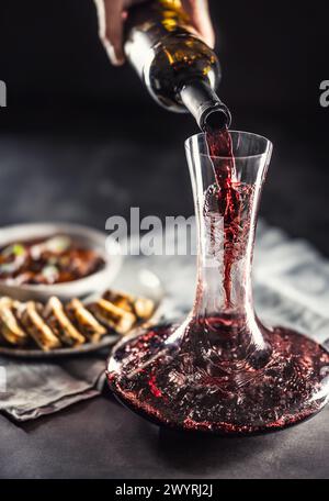 Rotwein wird aus einer Flasche in eine Karaffe auf einem Tisch gegossen, auf dem Wild, ungarisches oder Wiener Gulasch mit Karlovy Vary Klößchen zu finden sind. Stockfoto