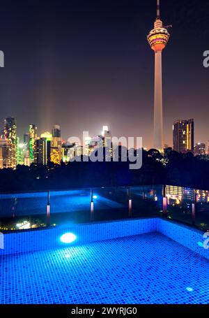 Atemberaubender Blick auf die Wolkenkratzer der Stadt KL, nachts hell beleuchtet, eleganter Pool im Vordergrund mit atemberaubendem Panoramablick Stockfoto