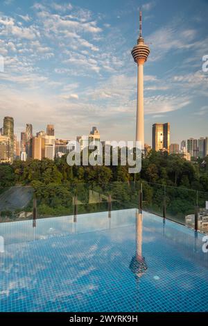 Atemberaubender Blick auf KL City und Menara Kuala Lumpur, in der Nähe des Sonnenuntergangs, mit blauem Infinity Pool auf der Dachterrasse im Vordergrund und blauem Himmel gesäumt Stockfoto