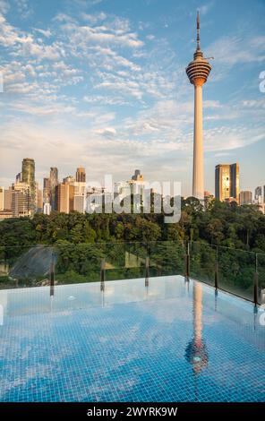 Atemberaubender Blick auf KL City und Menara Kuala Lumpur, in der Nähe des Sonnenuntergangs, mit blauem Infinity Pool auf der Dachterrasse im Vordergrund und blauem Himmel gesäumt Stockfoto