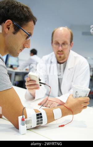 Forscher, der multipad Elektroden in den Kontrollarm für das Stimulationsmodell für Sensorsignale platziert Anwendungen für die Rehabilitation der unteren Extremität / des oberen Herzens / der Rückenmarksverletzung der Patient hat jetzt Krafttests, um einen Becher zu halten, Unit of Health Technology, Tecnalia Research & Innovation, Miramon Technology Park, San Sebastian, Donostia, Gipuzkoa, Baskenland, Spanien. Stockfoto