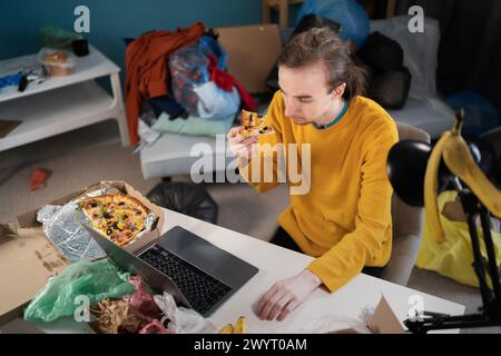 Student oder Freiberufler arbeiten und studieren in einem sehr chaotischen, überfüllten Raum mit vielen Klamotten Stockfoto