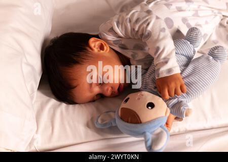 Baby schläft mit offenem Mund und kuschelt Teddybär im Bett Stockfoto