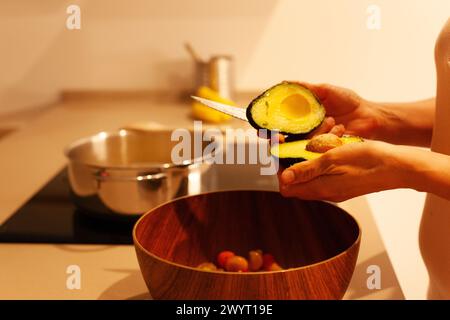 Frauenhände bereiten das Abendessen in der Küche vor und schneiden eine Avocado Stockfoto