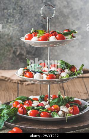 Klassischer italienischer Salat Insalata Caprese mit Kirschtomaten, Mini-Mozarella-Perlen, Basilikumblättern und Balsamglasur, serviert auf einem Kuchenstand, vertikal Stockfoto