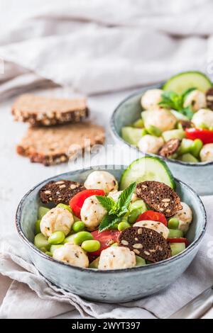 Sommersalat mit Gurke, Mini-Tomaten, Mini-Mozzarella und Sojabohnen auf weißem Holzhintergrund, vertikal Stockfoto