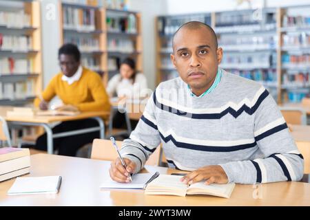 Junger erwachsener Mann, der in der öffentlichen Bibliothek studiert Stockfoto