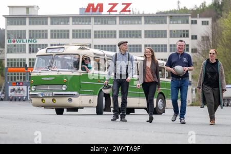 Zschopau, Deutschland. April 2024. Museumsdirektoren Dirk Schmerschneider (l-r), Museum für sächsische Fahrzeuge Chemnitz, Christiane Schlegel, Schloss Wildeck, Markus Schachtschneider, Deutsches Enduro Museum Zschopau und Patricia Meyn, Schloss Augustusburg, gehen Seite an Seite vor einem historischen Ikarus 55,51 Bus aus dem Jahr 1962 auf dem ehemaligen MZ Fabrikgelände in Zschopau. An vier Tagen in den kommenden Monaten können Interessenten die vier sächsischen Motorradmuseen im Oldtimer-Bus besuchen. Quelle: Hendrik Schmidt/dpa/Alamy Live News Stockfoto