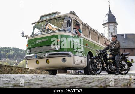 Zschopau, Deutschland. April 2024. Busfahrer Sven Mischke (l) und Dirk Schmerschneider vom Museum für Sächsische Fahrzeuge Chemnitz auf einem DKW SB 200 sprechen über einen historischen Ikarus-Bus 55,51 von 1962 im Innenhof von Schloss Wildeck. An vier Tagen in den kommenden Monaten können Interessenten die vier sächsischen Motorradmuseen im Oldtimerbus besuchen. Quelle: Hendrik Schmidt/dpa/Alamy Live News Stockfoto