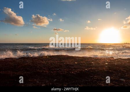 Sonnenuntergang über einem stürmischen Mittelmeer in Paphos, Zypern. Sandstrand, Winter, Sturmwolken am Himmel. Stockfoto