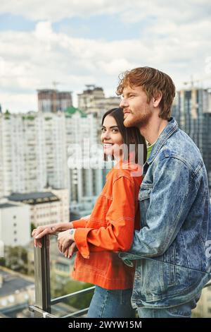 Ein Mann und eine Frau stehen auf einem Balkon mit Blick auf die Stadt, ihre Silhouetten vor dem Sonnenuntergang Stockfoto