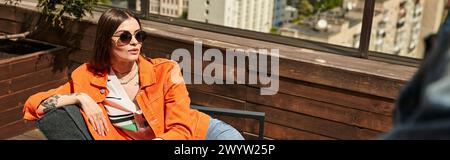 Eine Frau in einer orangen Jacke sitzt friedlich auf einer Holzbank und genießt einen Moment der Entspannung in einer ruhigen Umgebung im Freien Stockfoto