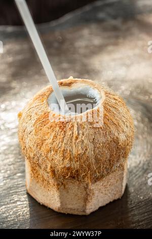 Kokosgetränk mit Strohhalm auf einem Holztisch. Tropisches frisches Kokoswasser mit Strohhalm. Erfrischender Kokoscocktail. Niemand, selektiver Fokus Stockfoto