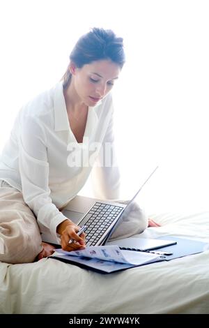Frau, die auf dem Bett sitzt und einen Laptop benutzt. Stockfoto