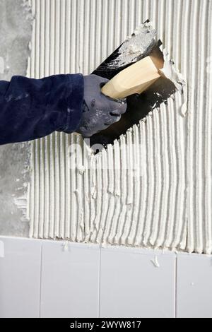Vorbereitung der Wand mit Klebmörtel vor dem Fliesen mit einer gezackten Putzkelle, Neubauten im Bau, Baustelle. Stockfoto