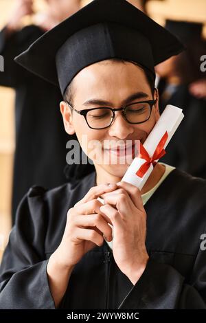 Asiatischer Mann mit Abschlussmütze und Kleid lächelnd, während er ein Diplom in der Hand hält. Stockfoto