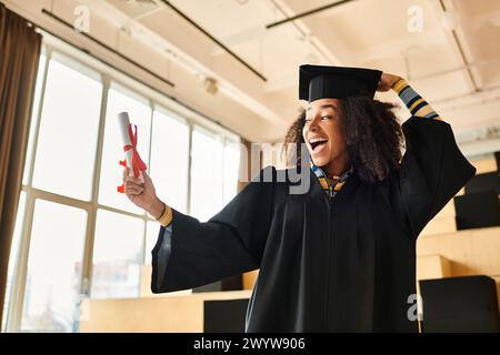Eine fröhliche Afroamerikanerin in einer Abschlussmütze und einem Kleid hält stolz ihr Diplom in einer feierlichen Atmosphäre hoch. Stockfoto