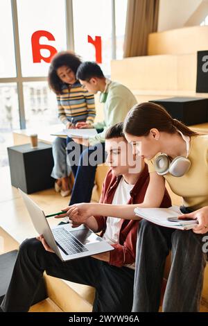 Multikulturelle Gruppe von Schülern, die auf der Bank sitzen, in Laptops vertieft sind und in Innenräumen arbeiten und zusammenarbeiten. Stockfoto