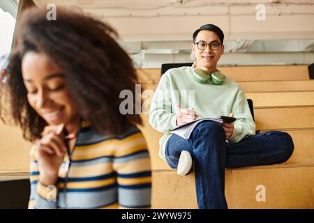 Ein schwarzes Mädchen und ein asiatischer Mann sitzen Seite an Seite auf einer Bank in einem multikulturellen Umfeld und symbolisieren Einheit und Vielfalt. Stockfoto