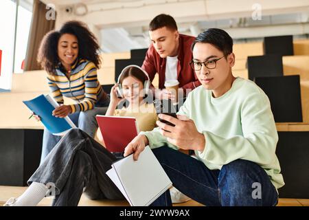 Multikulturelle Studenten sitzen, die Augen auf dem Handy fixiert und sich mit digitalen Inhalten beschäftigen Stockfoto