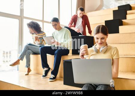 Multikulturelle Gruppe junger Menschen, die auf Treppen sitzen, sich auf Laptops konzentrieren und sich mit digitalem Lernen beschäftigen Stockfoto