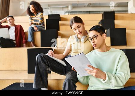 Ein Mann und eine Frau mit unterschiedlichem Hintergrund sitzen auf den Stufen des Vortragssaals, vertieft in Gespräche und Gedanken Stockfoto