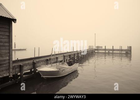 Ein monochromes/Sepia-Bild eines Bootes, das am Old Town Jetty an einem nebeligen Morgen auf dem Blackwood River in Augusta im Südwesten Westaustraliens vor Anker liegt. Stockfoto