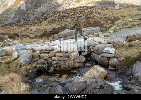 Frau, die über eine Steinbrücke geht, Llyn Idwal Path, Snowdonia National Park in der Nähe von Pont Pen-y-Benglog, Bethesda, Bangor, Wales, Großbritannien Stockfoto