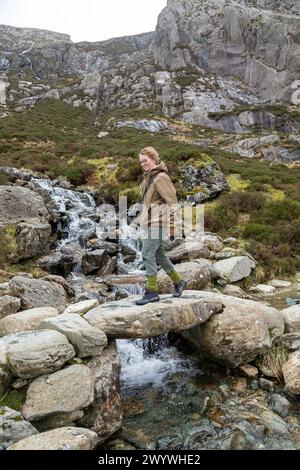 Frau, die über eine Steinbrücke geht, Llyn Idwal Path, Snowdonia National Park in der Nähe von Pont Pen-y-Benglog, Bethesda, Bangor, Wales, Großbritannien Stockfoto