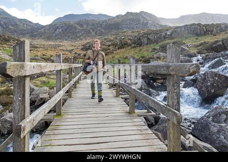 Frau, die über die Brücke geht, Llyn Idwal Path, Snowdonia National Park in der Nähe von Pont Pen-y-benglog, Bethesda, Bangor, Wales, Großbritannien Stockfoto