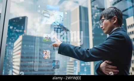 Eleganter japanischer Geschäftsmann, der mit dem futuristischen, fortschrittlichen holografischen Bildschirm im Aufzug durch die Nachrichten scannt. Succesful Male fährt zum Büro im modernen Buisness Center. Stockfoto