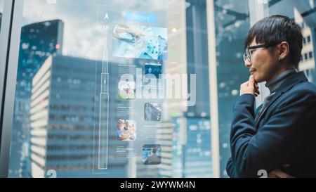 Eleganter japanischer Geschäftsmann, der mit dem futuristischen, fortschrittlichen holografischen Bildschirm im Aufzug durch die Nachrichten scannt. Succesful Male fährt zum Büro im modernen Buisness Center. Stockfoto