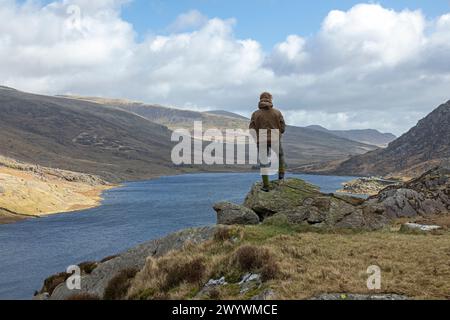 Frau auf Felsen mit Blick auf den Lake Llyn Ogwen, Snowdonia National Park in der Nähe von Pont Pen-y-Benglog, Bethesda, Bangor, Wales, Großbritannien Stockfoto