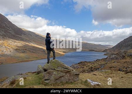 Mann auf Felsen mit Blick auf den Lake Llyn Ogwen, Snowdonia National Park in der Nähe von Pont Pen-y-Benglog, Bethesda, Bangor, Wales, Großbritannien Stockfoto