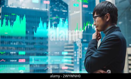 Eleganter japanischer Geschäftsmann, der den Börsenmarkt mit futuristischem, fortschrittlichem holografischem Bildschirm im Aufzug studiert. Succesful Male fährt zum Büro im modernen Buisness Center. Stockfoto
