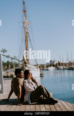 Ein Paar sitzt nahe an einem Dock und genießt einen ruhigen Moment mit Blick auf den Yachthafen an einem sonnigen Tag in Barcelona. Stockfoto