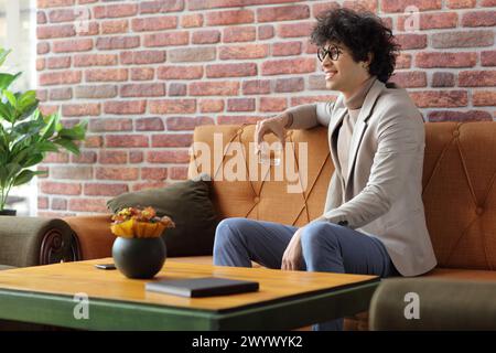 Junger Mann in einem Café, der ein Glas mit Whiskey hält und durch ein Fenster schaut Stockfoto