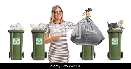 Junge Frau, die auf einen Müllsack vor Mülltonnen zeigt, isoliert auf weißem Hintergrund Stockfoto