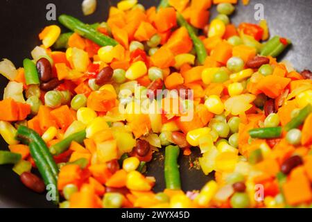 Löffel rührt ein Gemisch Gemüse in einer brausenden Pfanne kräftig um, wodurch eine Symphonie aus Farben und Aroma entsteht. Stockfoto