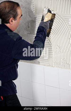 Vorbereitung der Wand mit Klebmörtel vor dem Fliesen mit einer gezackten Putzkelle, Neubauten im Bau, Baustelle. Stockfoto