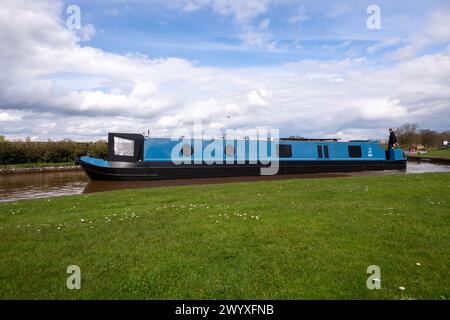 Brandneues blaues Schmalboot, gebaut von Knights Schmalbooten aus Cheshire, das an einem hellen Frühlingstag aus einem Yachthafen auf den Shropshire Union Canal gefahren wird. Stockfoto