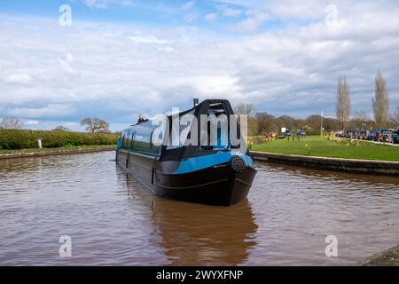 Brandneues blaues Schmalboot, gebaut von Knights Schmalbooten aus Cheshire, das an einem hellen Frühlingstag aus einem Yachthafen auf den Shropshire Union Canal gefahren wird. Stockfoto