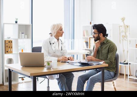 Kaukasische Oberärztin und junger Hustenmännlicher Patient am Tisch. Stockfoto