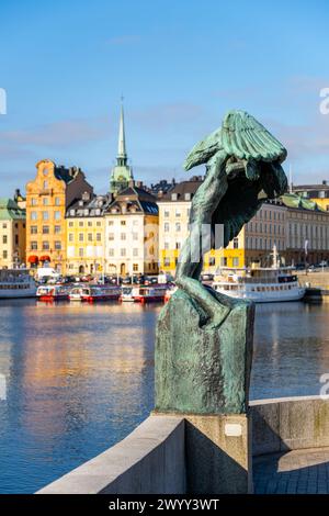 Flügel - eine Bronzeskulptur steht an der Skeppsholmen Bridge mit Blick auf farbenfrohe Gebäude und Boote entlang des Stockholmer Ufers unter klarem blauen Himmel. Stockholm, Schweden Stockfoto