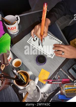 Ein jüngerer Junge zeichnet arabische Kalligraphie, schließt muslimische Jungen Hände, die arabischen Text mit Bambusstiften und schwarzer Tinte auf Papier schreiben Stockfoto